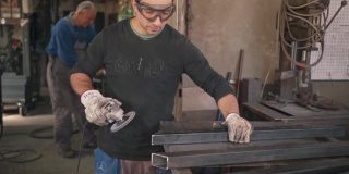 中年的专业焊工在他的焊接车间里打磨一根金属棒