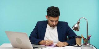 专注的商人坐在办公室的记事本上做笔记，在笔记本电脑上寻找创意，为创业工作