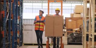 亚洲女经理拿着剪贴板检查清单存货和工人使用手堆垛机一起走在仓库。