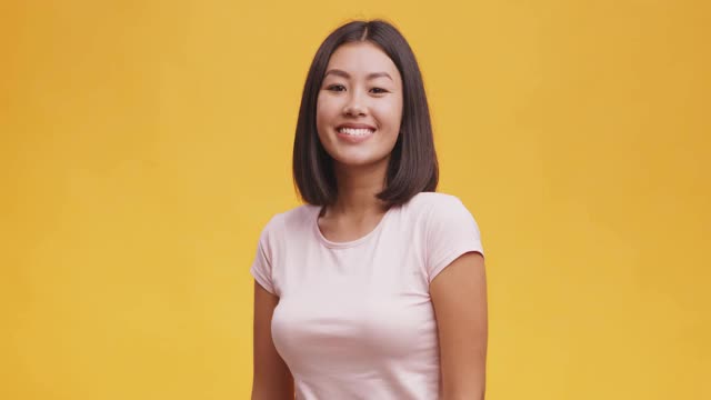 工作室肖像年轻可爱的亚洲女士，整理头发和微笑的相机，橙色的背景
