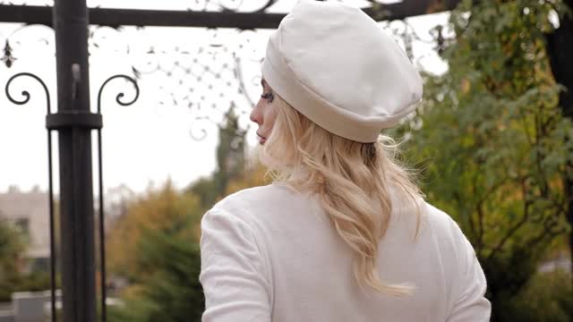 一名年轻女子带着明亮的妆容和白色的复古帽子在城市公园里摆姿势。