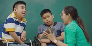 亚洲身体残疾的小男孩学生坐在轮椅上在课堂上学习老师正在使用平板电脑教学。残疾儿童技能培训学习技术