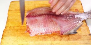 用手把去皮的咸鱼干切成片放在木板上。