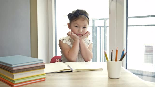 小女孩双手托着头，若有所思地坐着。回到学校