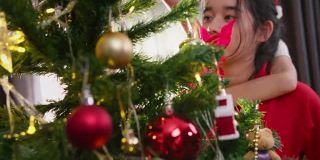 一个亚洲少女和她的哥哥姐姐在圣诞节的时候在家里的客厅里装饰圣诞树。