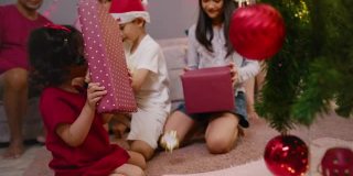 亚洲少女惊喜礼物盒给她可爱的哥哥和妹妹，而庆祝她的家人在圣诞节假期在家里的客厅。四个兄弟姐妹拥抱和微笑。