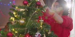 在圣诞节期间，在家里的客厅里装饰圣诞树。美女挂红球。