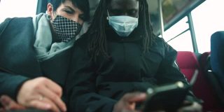 一名戴面具的黑人男子和一名戴面具的白人女子在公交车上看手机屏幕。