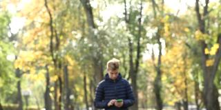 一个年轻的帅哥在秋天的公园里边走边用手机。在公园里，人们边走边看在线新闻，用智能手机在社交网络上发短信。