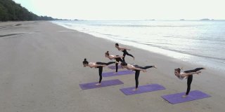 鸟瞰图的团队身体战斗群做瑜伽在一个阳光灿烂的一天在海滩上。