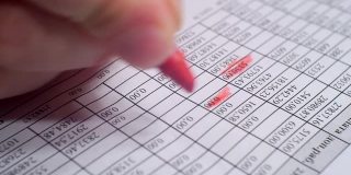 手用红色记号笔在一张写有财务信息的纸上做笔记