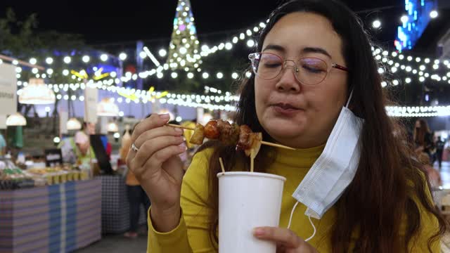 4K，亚洲妇女吃泰国街头食物叫猪肉烤木托盘在夜市的人走