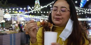 4K，亚洲妇女吃泰国街头食物叫猪肉烤木托盘在夜市的人走