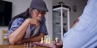 亚洲资深男士朋友在家里客厅下棋，积极的资深人士理念