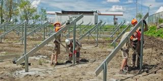 太阳能电池板的金属结构。夏天，戴着防护帽的工人们在田里建造新的太阳能农场。