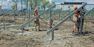 工程师把金属建筑放在地上。夏天，一群戴着安全帽的工人在田里为太阳能电池板搭建金属底座。