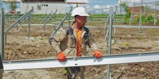 户外太阳能农场的建筑工地。戴安全帽的工人扛着金属框架在现场工作。