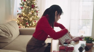 年轻女子在圣诞节期间在家包装圣诞礼物。视频素材模板下载