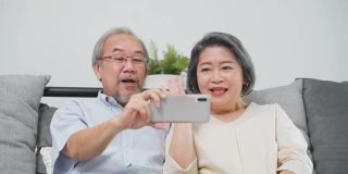 亚洲老年妇女和老人手持手机或平板电脑，在家里与儿子、女儿、孙子、孙女进行视频通话和微笑。祖父母对通过互联网交流感到高兴。