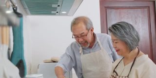 夫妇老亚洲长者幸福生活在家庭厨房。爷爷和奶奶一起煮沙拉菜，快乐地微笑着一起享受退休生活。老年人的关系和活动。