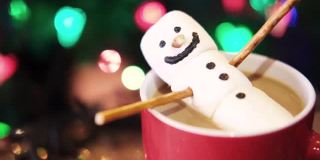 可食用雪人的软糖棉花糖在巧克力牛奶的圣诞花环散景背景与文字的地方。婴儿食品的概念为圣诞节和可食用的装饰新年