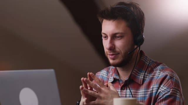 自信的男人戴着耳机在网上视频会议上讲话，在遥远的工作场所用手势解释项目