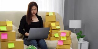 女企业家使用笔记本电脑，并检查准备递送给客户在家办公的包裹盒子，(中小企业业务)