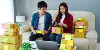 夫妇网上企业家用胶带打包包裹盒子在家里的办公室，准备产品交付给客户，(中小企业)