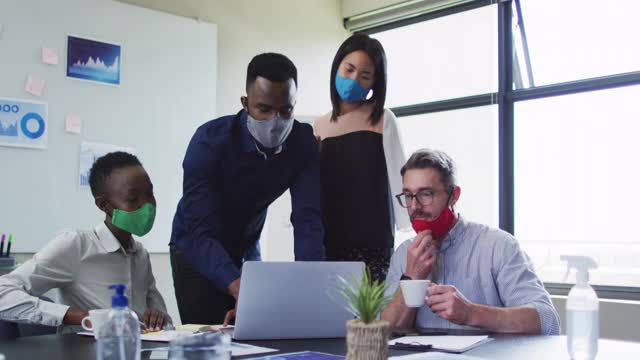 在现代办公室的会议室里，同事们戴着口罩一起使用笔记本电脑