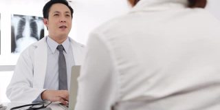 严肃的亚洲男医生正在用笔记本电脑传送好消息，谈论结果或症状与女病人坐在医院办公室的桌子前。