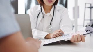 年轻的亚洲女医生正在用剪贴板传递好消息，谈论结果或症状与男性病人坐在健康诊所的桌子上。视频素材模板下载