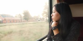 亚洲女性在乘坐公共交通工具时，坐在火车上看窗外的风景。4 k慢动作。