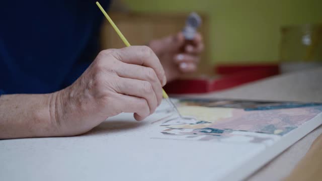 在冠状病毒隔离和封锁期间学习新的爱好。资深女艺术家在家作画。迷人的老妇人画画，做她最喜欢的爱好。老年妇女感到鼓舞。