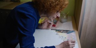 在冠状病毒隔离和封锁期间学习新的爱好。资深女艺术家在家作画。迷人的老妇人画画，做她最喜欢的爱好。老年妇女感到鼓舞。