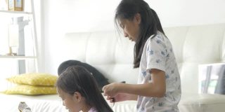 手亚洲女孩在家里编她的姐姐的头发，孩子一起玩，生活理念。