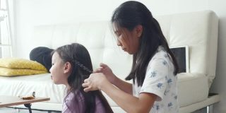 手亚洲女孩在家里编她的姐姐的头发，孩子一起玩，生活理念。