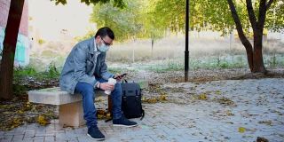 一名戴着面具的男子坐在公园的长凳上看手机