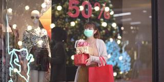 亚洲妇女戴着防护面具在购物中心拿着礼盒