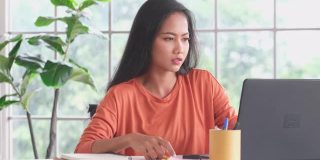 年轻的亚洲女子疲惫的工作与笔记本电脑在家里办公室，从家里工作