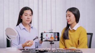 年轻的亚洲女性制作视频，为自己的博客上的化妆品现在的产品和直播视频到社交网络通过互联网在家庭美容博客的概念视频素材模板下载