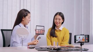 年轻的亚洲女性制作视频，为自己的博客上的化妆品现在的产品和直播视频到社交网络通过互联网在家庭美容博客的概念视频素材模板下载