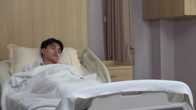 年轻的亚洲医生和护士在医院医务室的病床上用听诊器检查男病人的心肺