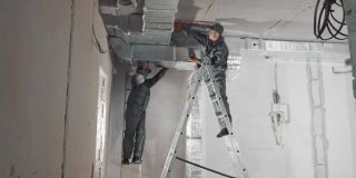 为新房子安装通风系统的雇员。船长站在梯子上，安装固定在天花板上的煤气管道和管网。