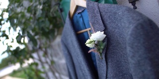 一件灰色的男式西装上衣，衣架上挂着一个胸花