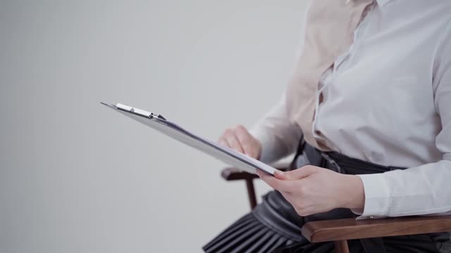女人手里的文件夹。女商人穿着白色衬衫坐在椅子上看书。特写镜头。缓慢的运动。