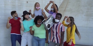 快乐的朋友戴着面具听音乐与老式扬声器户外-多种族的年轻人在冠状病毒爆发期间一起欢乐跳舞