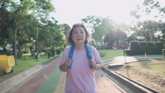 亚洲资深妇女慢跑公园在一个阳光明媚的日子在慢镜头。退休健康生活活动