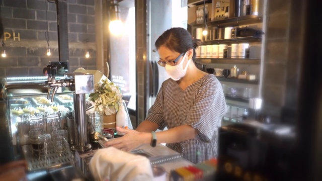 两名亚洲妇女戴着防护口罩在咖啡店用智能手机付款