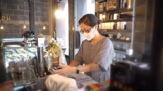 两名亚洲妇女戴着防护口罩在咖啡店用智能手机付款视频素材模板下载
