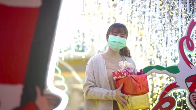 亚洲妇女戴着防护面具，拿着一个礼盒在led灯